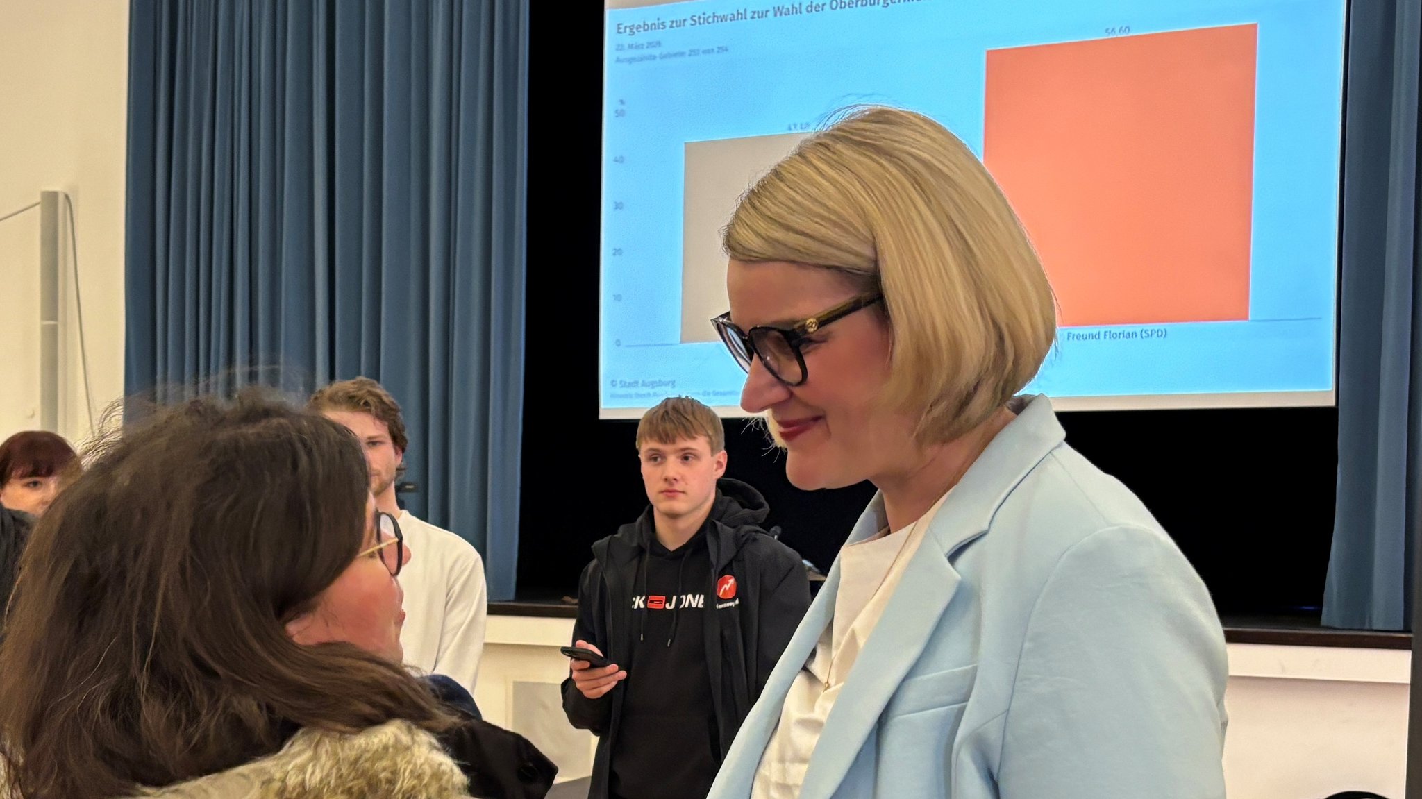 Die Augsburger Oberbürgermeisterin Eva Weber (CSU) im Gespräch mit einer Frau; im Hintergrund das Wahlergebnis auf eine Leinwand projiziert. Die Augsburger Oberbürgermeisterin Eva Weber (CSU) hat die Stichwahl gegen Florian Freund (SPD) verloren.