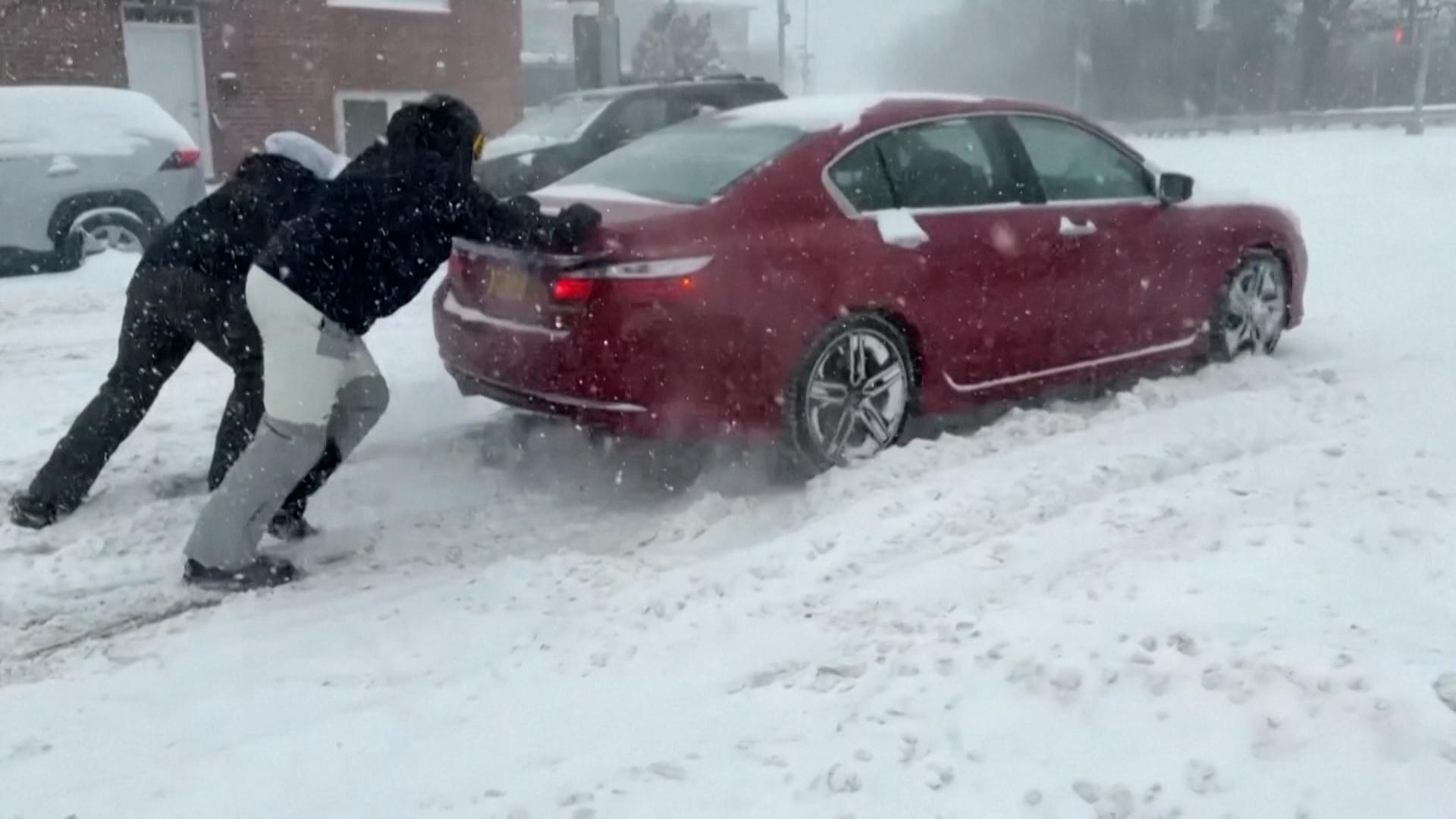 Zwei Männer schieben ein Auto im Schnee an.