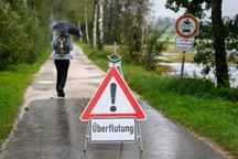 Dauerregen in Bayern: Eine Frau geht bei Felden am Chiemsee an einem Schild mit der Aufschrift „Überflutung“ vorbei. | Bild:picture alliance/dpa/Lennart Preiss