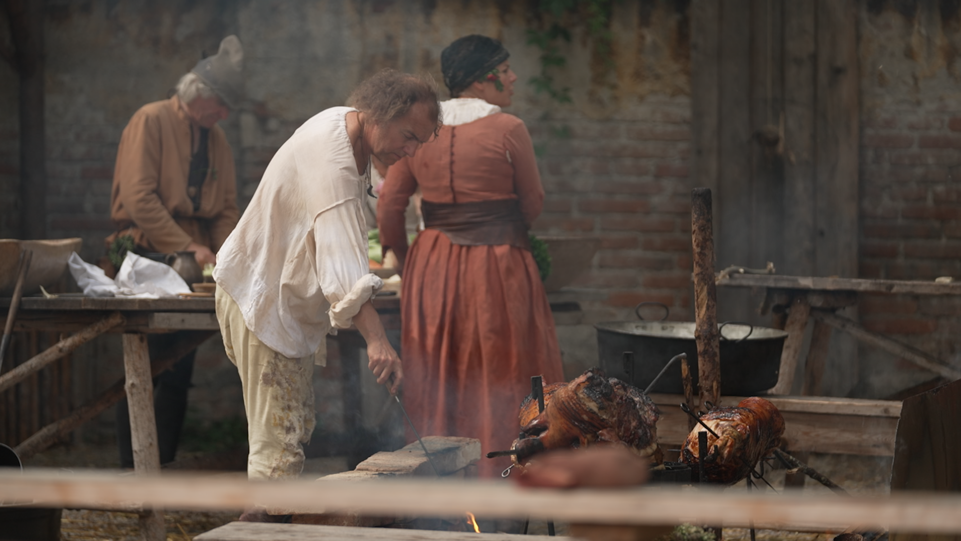 Koch in mittelalterlicher Kleidung bereitet ein Spanferkel zu