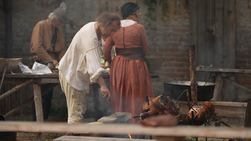 Koch in mittelalterlicher Kleidung bereitet ein Spanferkel zu