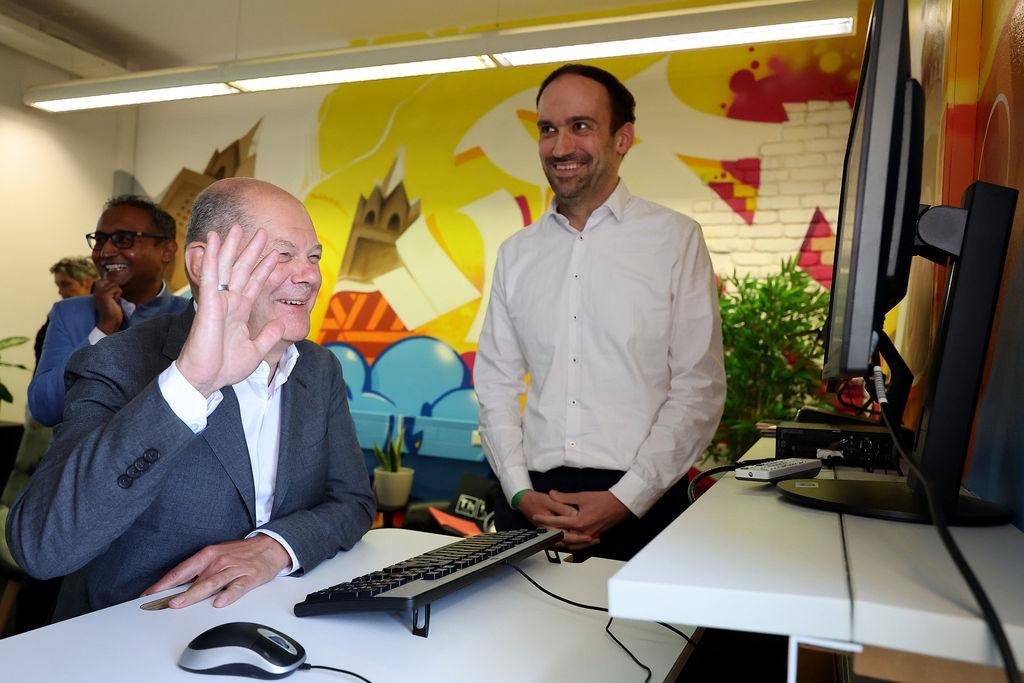 08.07.2024, Bayern, Nürnberg: Bundeskanzler Olaf Scholz (SPD, vorn) besucht das Bundesamt für Migration (BAMF) und unterhält sich mit Johannes Wenisch (r), Leiter für den Bereich Künstliche Intelligenz. Dahinter lächelt Kausik Munsi, Abteilungsleiter digitale Technologien. Scholz informierte sich über die aktuelle Situation bei den Asylverfahren in Deutschland. Das Bundesamt arbeitet angesichts der Vielzahl der Anträge an der Kapazitätsgrenze. Foto: Daniel Löb/dpa Pool/dpa +++ dpa-Bildfunk +++