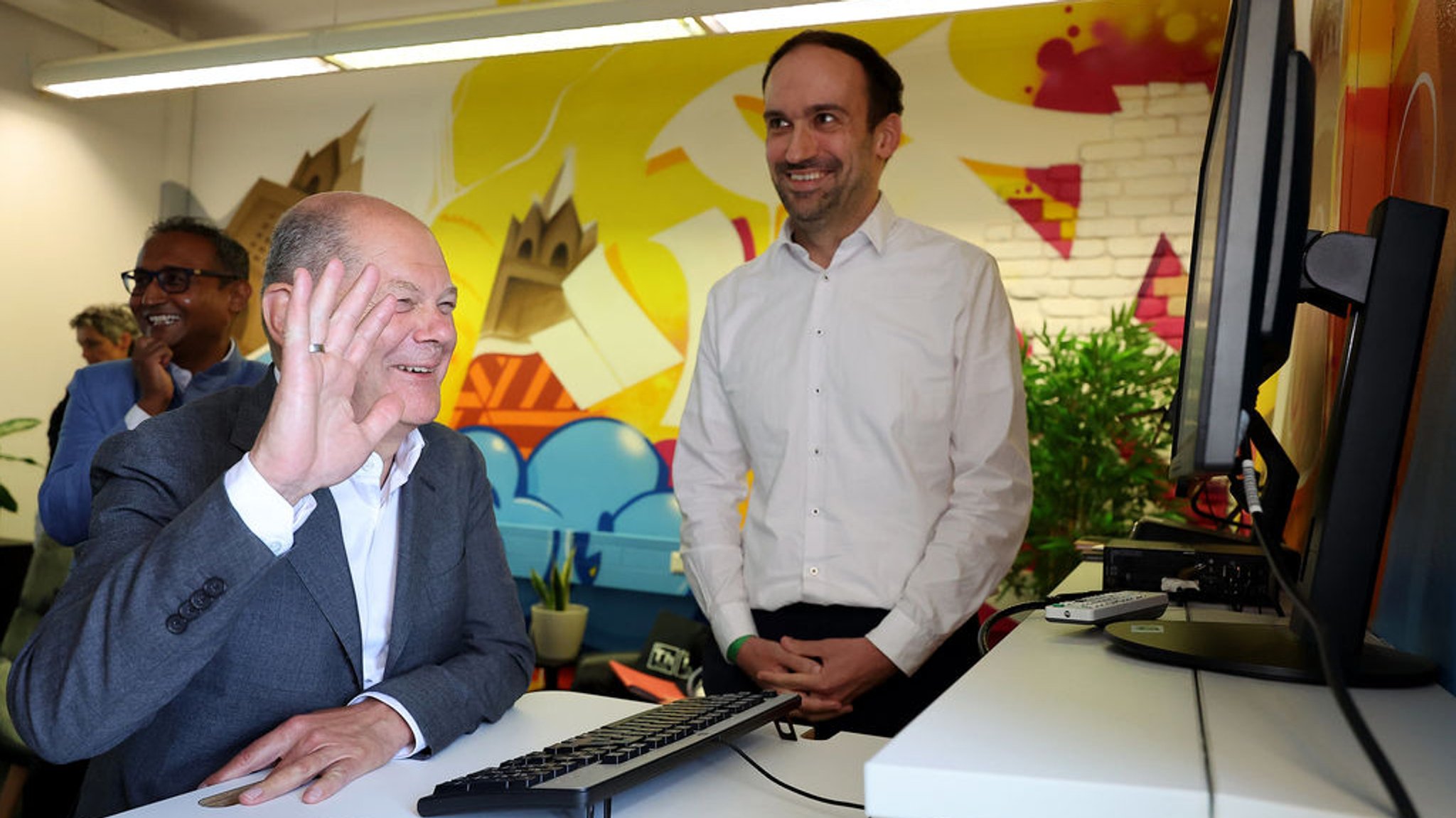 08.07.2024, Bayern, Nürnberg: Bundeskanzler Olaf Scholz (SPD, vorn) besucht das Bundesamt für Migration (BAMF) und unterhält sich mit Johannes Wenisch (r), Leiter für den Bereich Künstliche Intelligenz. Dahinter lächelt Kausik Munsi, Abteilungsleiter digitale Technologien. Scholz informierte sich über die aktuelle Situation bei den Asylverfahren in Deutschland. Das Bundesamt arbeitet angesichts der Vielzahl der Anträge an der Kapazitätsgrenze. Foto: Daniel Löb/dpa Pool/dpa +++ dpa-Bildfunk +++