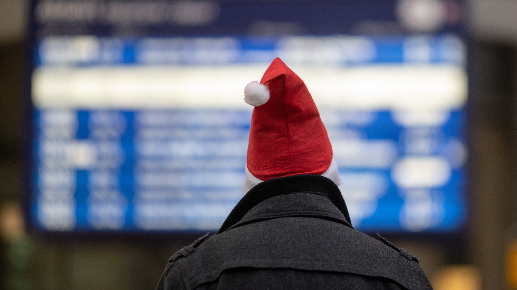 Ein Mann mit einer roten Weihnachtsmütze schaut auf Anzeigentafeln am Bahnhof.