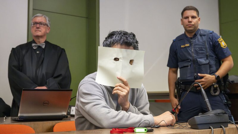 19.05.2025, Bayern, München: Der Angeklagte sitzt zum Prozessauftakt auf seinem Platz im Gerichtssaal des Landgerichts München und verdeckt sein Gesicht. Die Bundesanwaltschaft wirft dem Angeklagten und seiner Frau Völkermord, Verbrechen gegen die Menschlichkeit und Kriegsverbrechen sowie die Mitgliedschaft in der Terrormiliz «Islamischer Staat» vor. Foto: Peter Kneffel/dpa +++ dpa-Bildfunk +++ | Bild: dpa-Bildfunk/Peter Kneffel 19.05.2025, Bayern, München: Der Angeklagte sitzt zum Prozessauftakt auf seinem Platz im Gerichtssaal des Landgerichts München und verdeckt sein Gesicht. Die Bundesanwaltschaft wirft dem Angeklagten und seiner Frau Völkermord, Verbrechen gegen die Menschlichkeit und Kriegsverbrechen sowie die Mitgliedschaft in der Terrormiliz «Islamischer Staat» vor. Foto: Peter Kneffel/dpa +++ dpa-Bildfunk +++