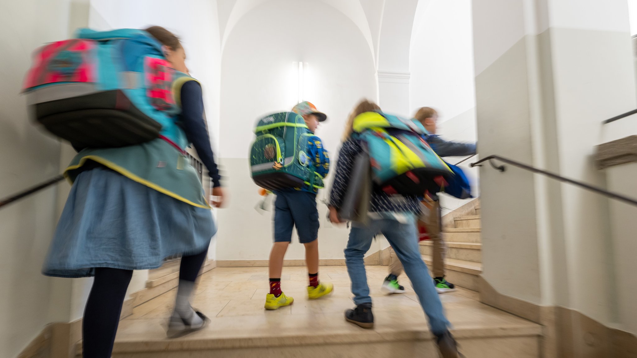 Symbolbild: Kinder mit Schulranzen laufen die Treppe einer Grundschule hoch.