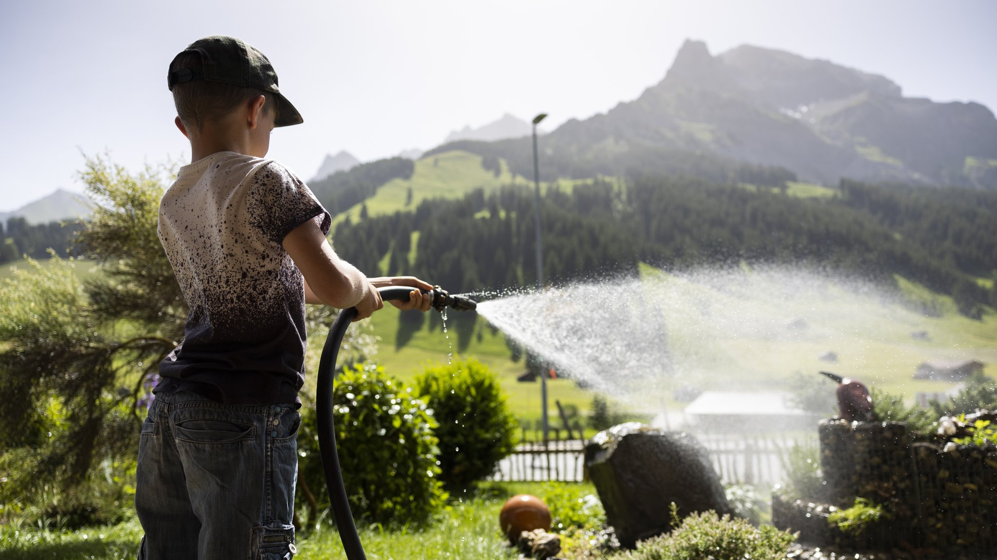 Junge in der Schweiz gießt die Blumen im Garten