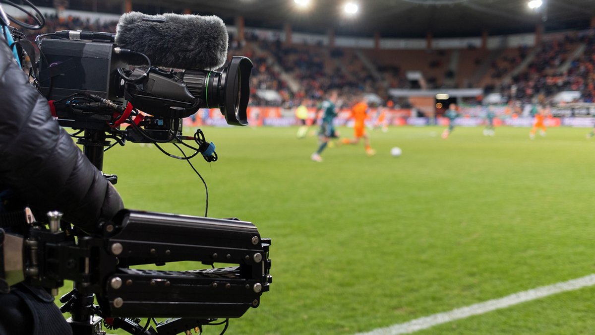 Symbolbild TV-Rechte: Ein Kameramann steht hinter seiner Kamera am Rande eine Fußballplatzes.