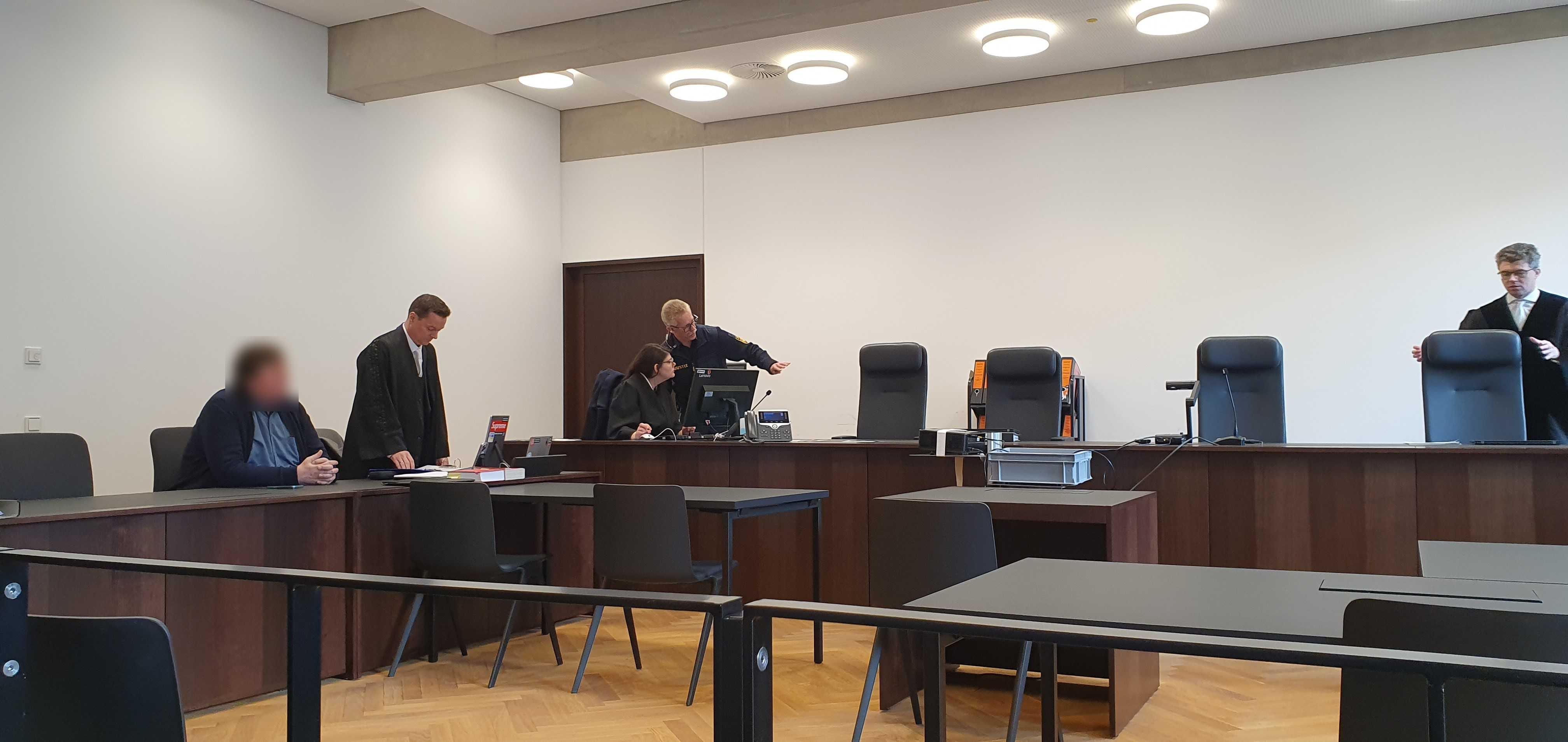 Der Angeklagte, sein Verteidiger und weitere Personen befinden sich in einem Gerichtssaal.