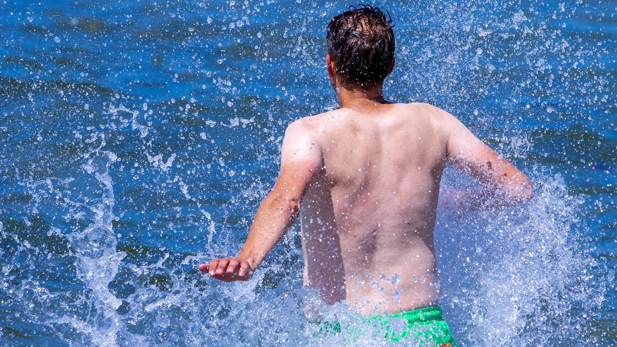 Urlauber in Warnemünde rennt in die noch kühle Ostsee. Steigen die Temperaturen, wie von der Weltwetterorganisation (WMO) vorhergesagt, könnte ein Bad in der Ostsee aufgrund spezieller Bakterien diesen Sommer gefährlich werden.