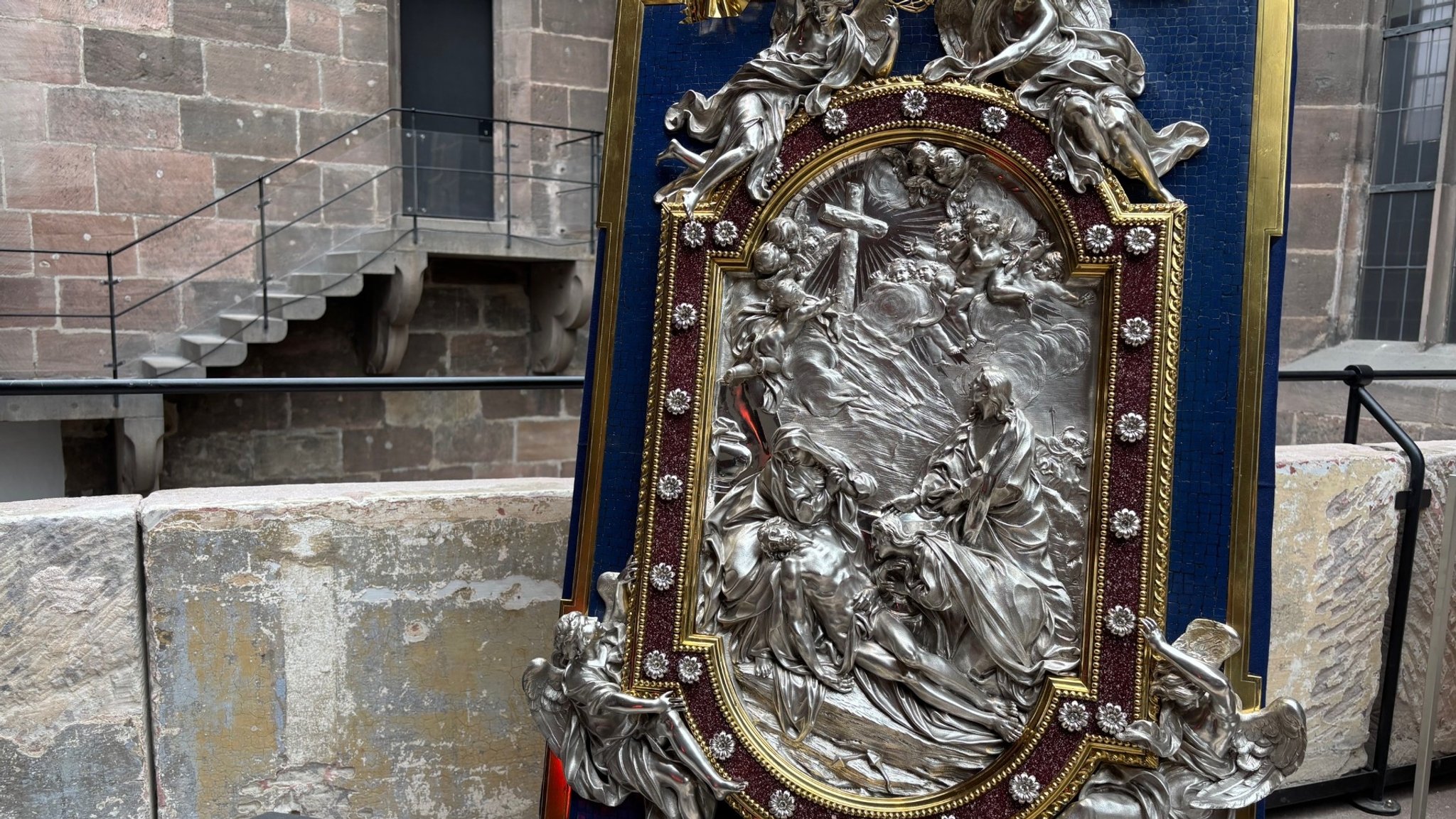 Ein prächtiges Silberrelief in einem dunkelblau-goldenen Rahmen ist an eine Wand gelehnt. 