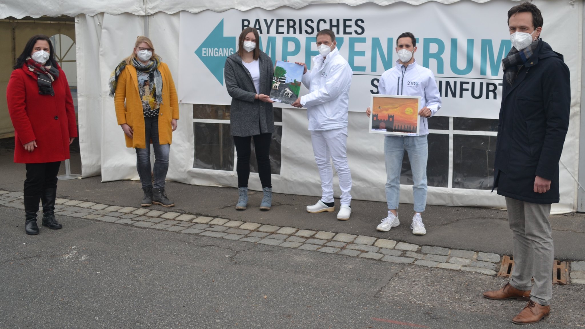 Die Bilderübergabe am Impfzentrum in Schweinfurt mit (von links) Rektorin Nicole Schmitt, Fachlehrerin Christina Düring, Schülerin Laura Hackenberg (alle Balthasar-Neumann-Mittelschule Werneck), Dr. Markus Hüttl, Felix Weisheit (beide Firma 21 Dx) sowie Landrat Florian Töpper.