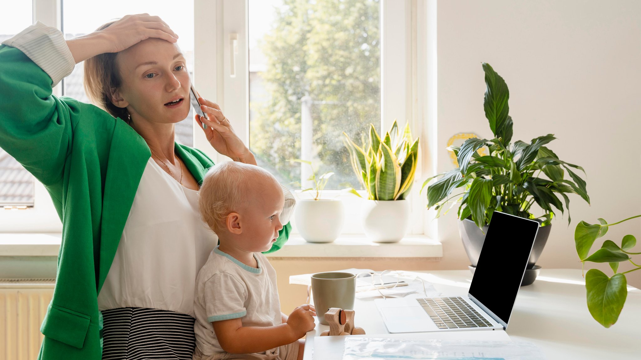 Eine Mutter sitzt mit ihrem Kleinkind auf dem Schoß am Laptop und telefoniert. Eine Vier-Tage Woche bedeutet oft längere Arbeitstage.