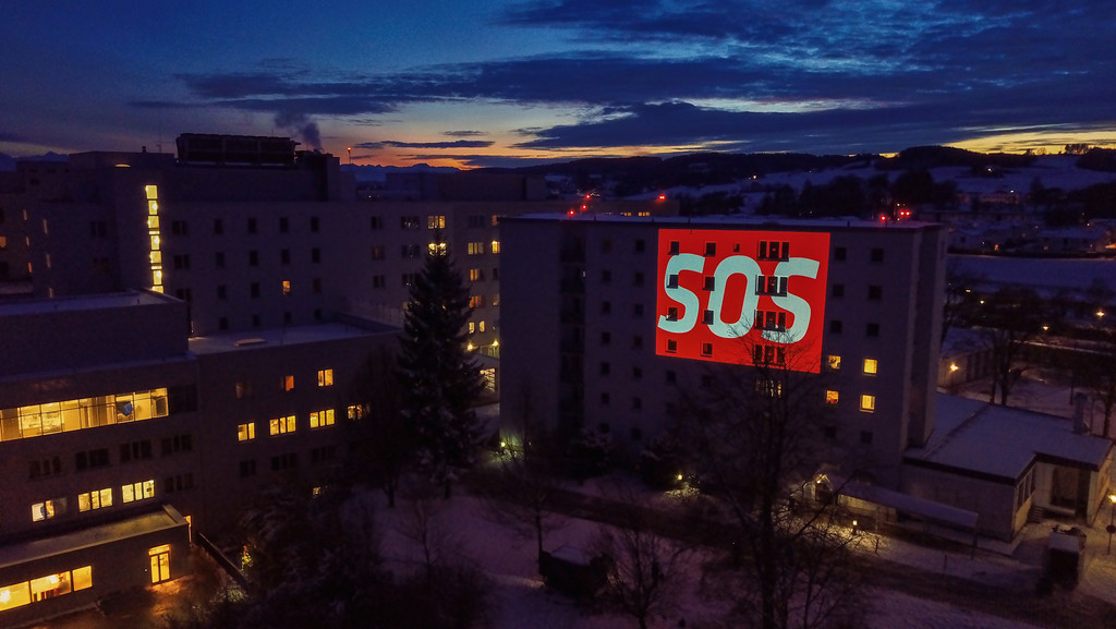 Luftbild des Klinikums Kaufbeuren vom Dezember 2021 mit dem rot-weißen Schriftzug "SOS", der an die Fassade projiziert wurde. 
