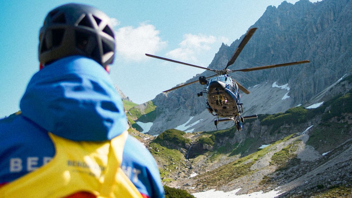Ein Hubschrauber landet in den Bergen, während ein Bergretter von der Bergwacht Allgäu am Boden wartet.
