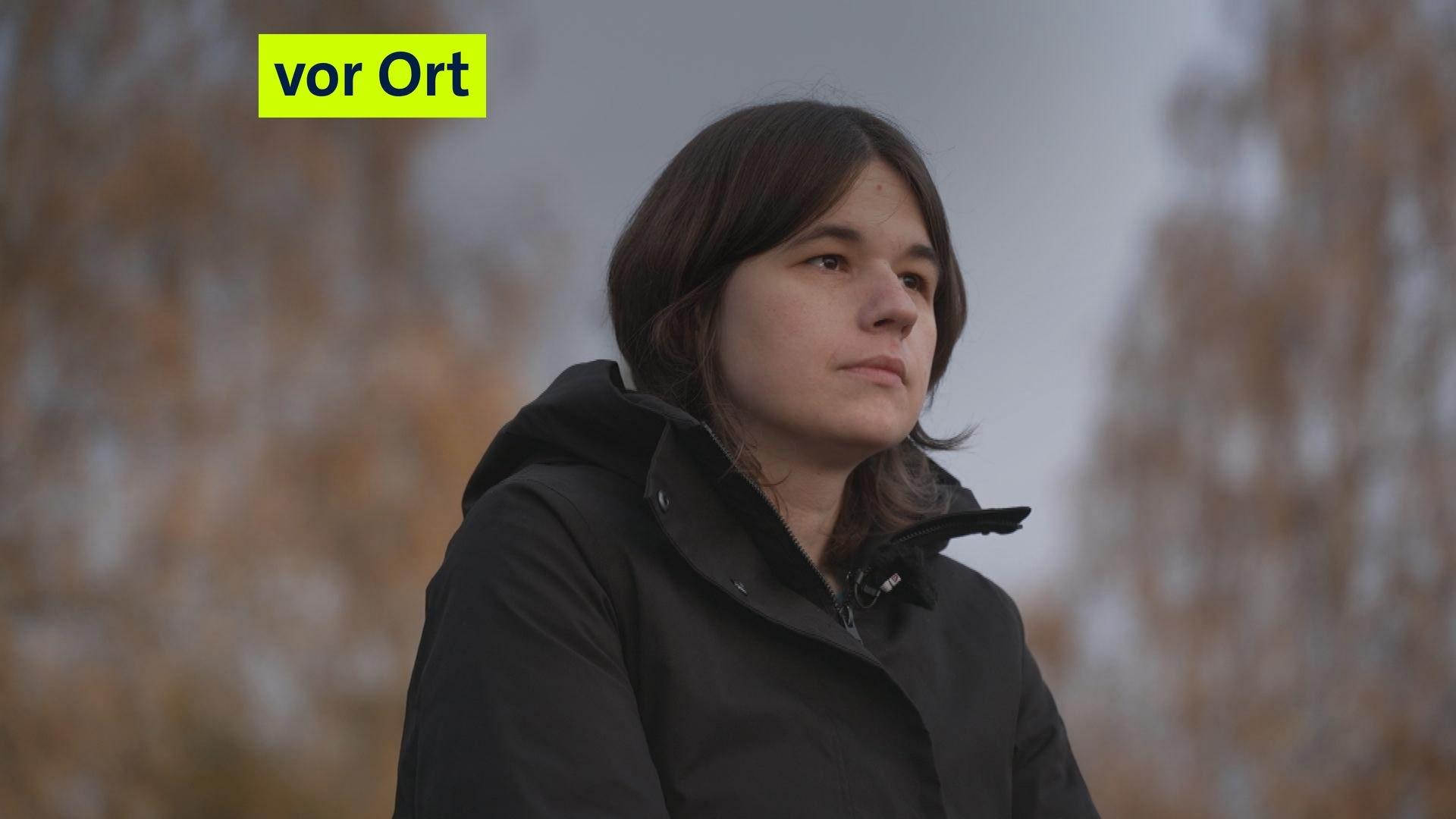 Eine Frau mit einer schwarzen Jacke und braunen Haaren guckt in die Ferne. 