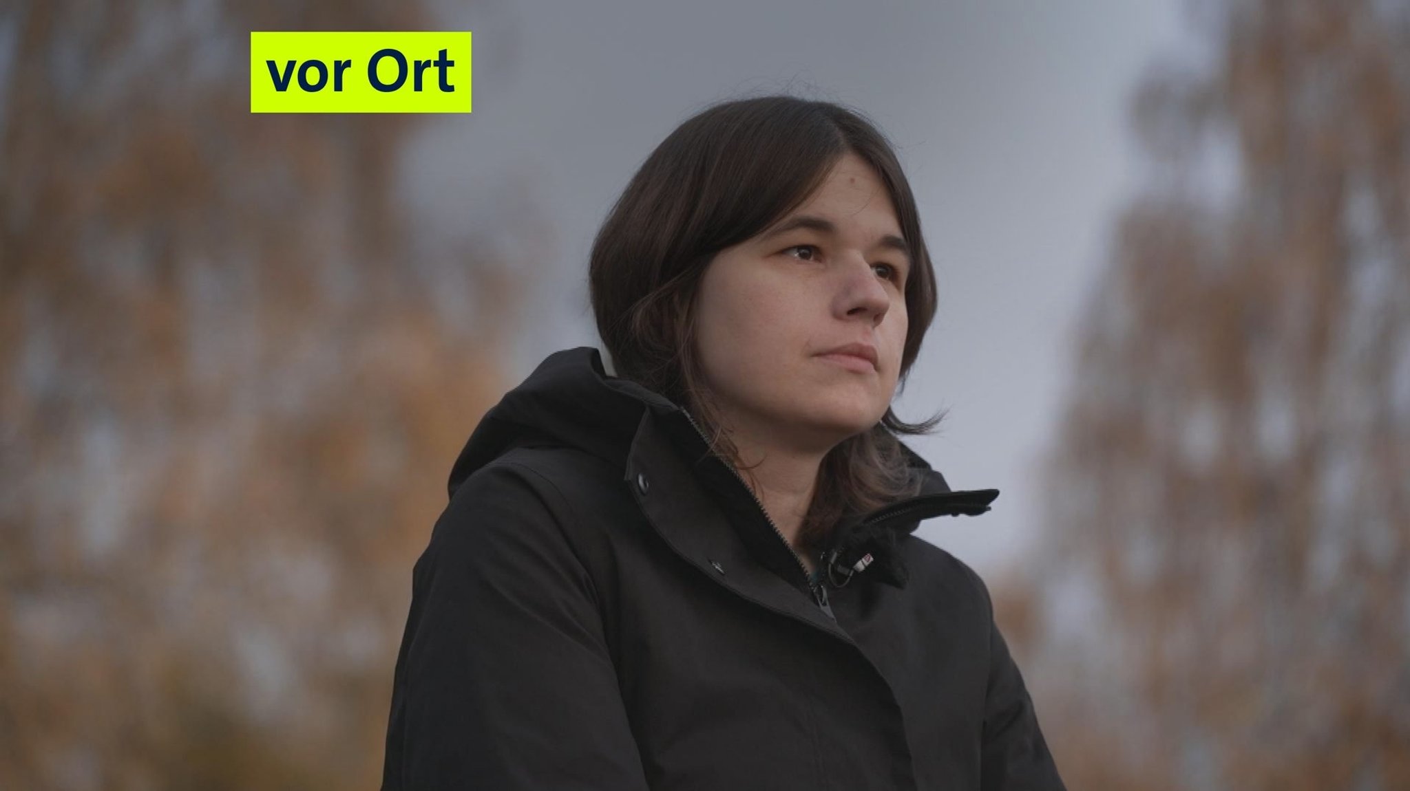 Eine Frau mit einer schwarzen Jacke und braunen Haaren guckt in die Ferne. 