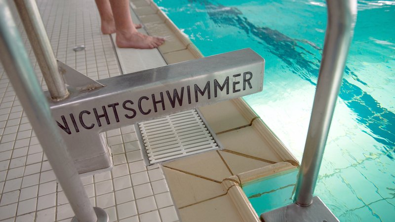 Ein Bademeister steht in einem Hallenbad neben einem Nichtschwimmerschild.