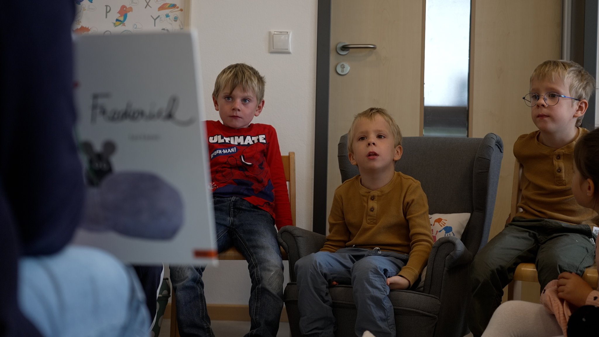 Kinder sitzen auf kleinen Stühlen im Kindergarten und lauschen einer Vorleserin | Bild: Nadine Cibu/BR Kinder sitzen auf kleinen Stühlen im Kindergarten und lauschen einer Vorleserin