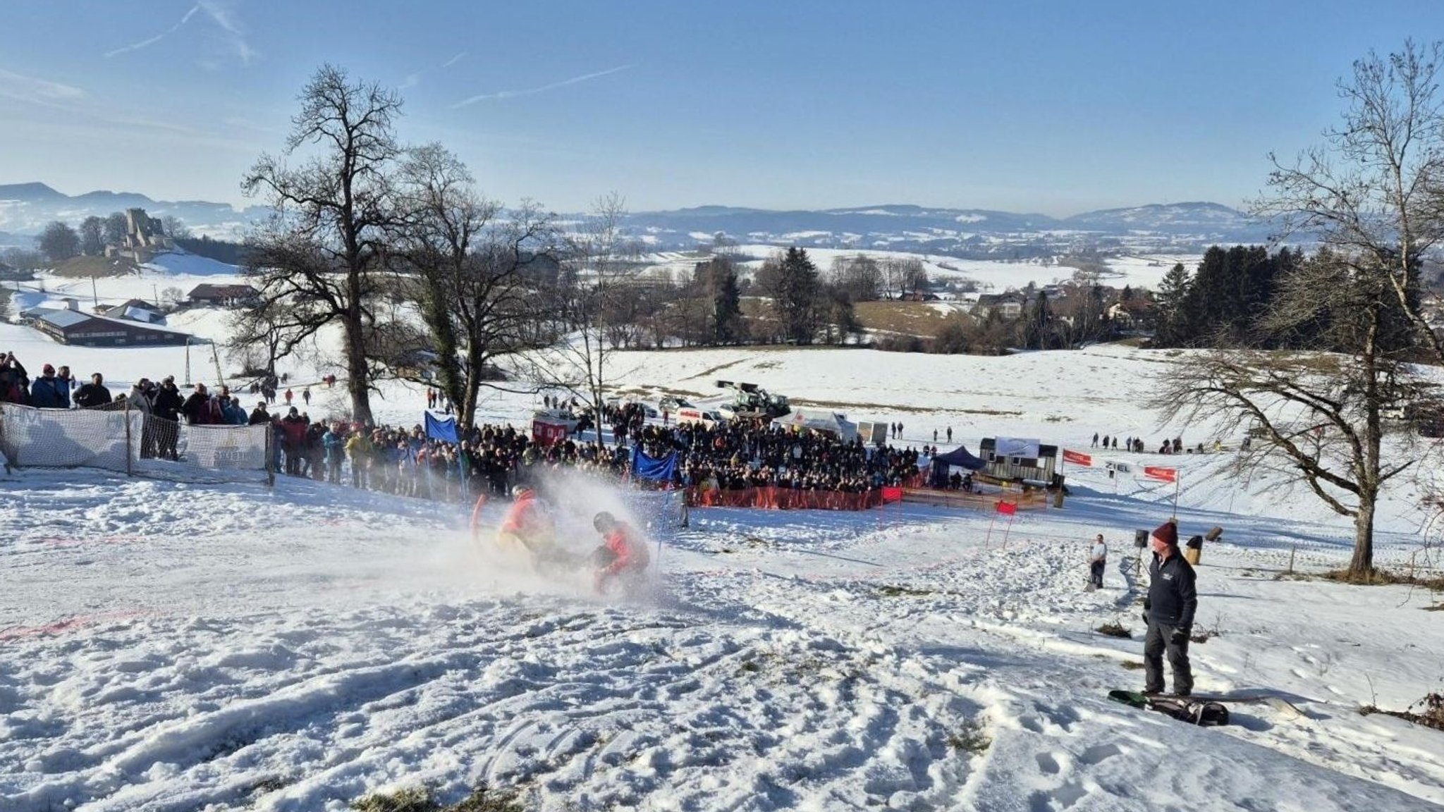 Ein verschneiter Berghang, auf dem ein etwas größerer Schlitten mit zwei Personen drauf sehr schnell fährt. | Bild: BR / Christian M. Hammer Ein verschneiter Berghang, auf dem ein etwas größerer Schlitten mit zwei Personen drauf sehr schnell fährt.