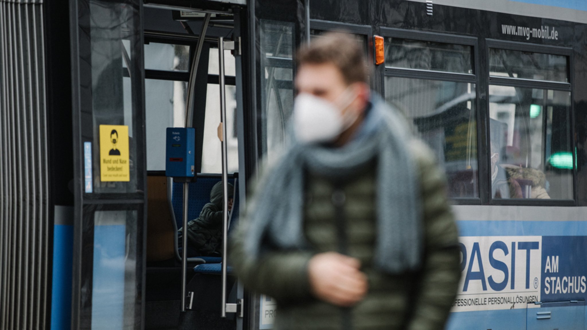 Ein Mann mit einer FFP2-Maske an einer Tramhaltestelle.