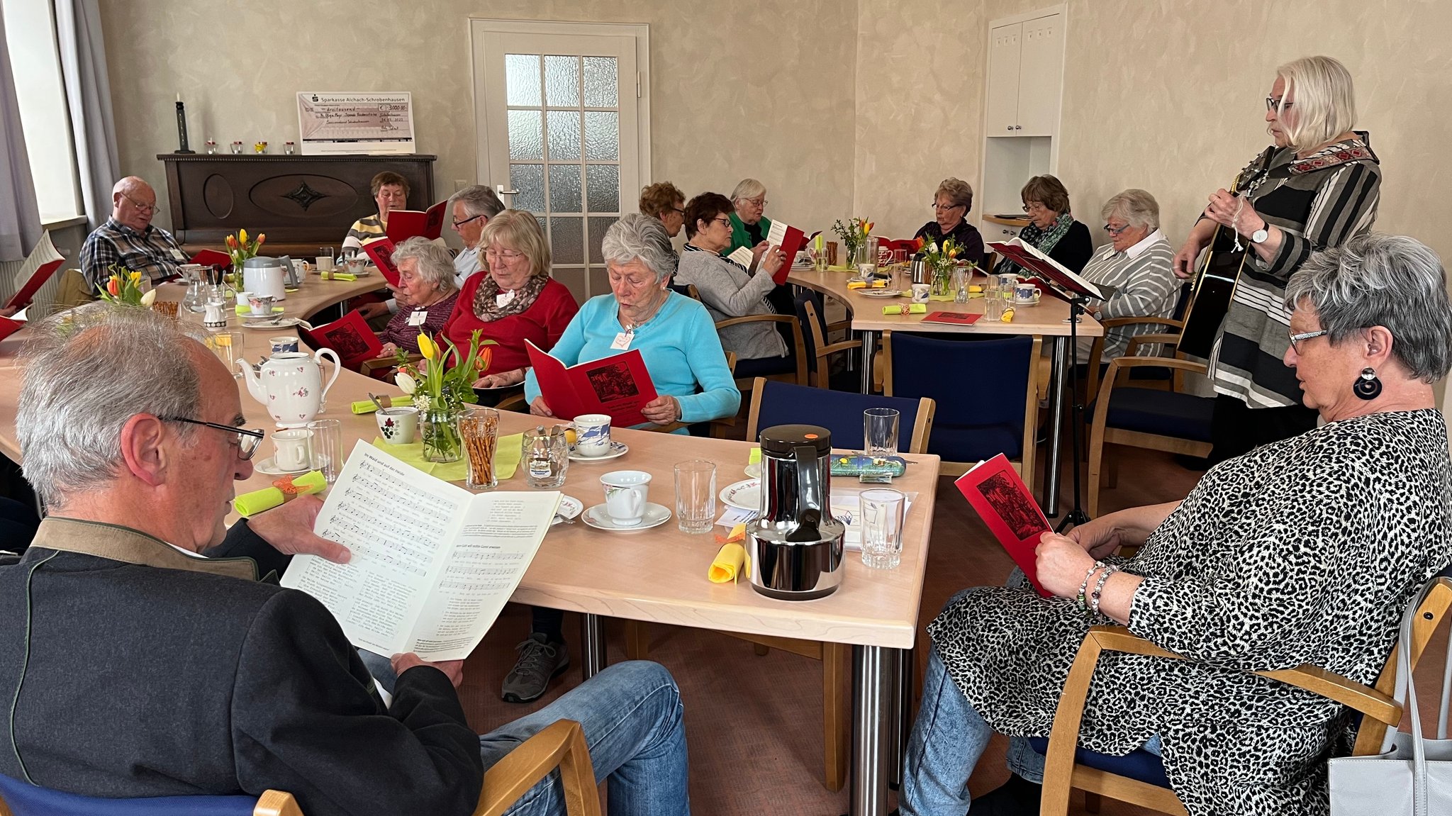 Die Seniorinnen und Senioren sitzen mit Liederheften da und singen mit Gitarrenbegleitung.