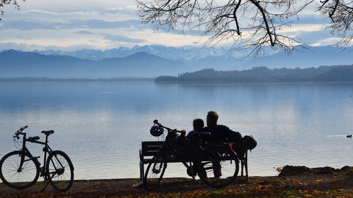 Ein Paar mit sitzt auf einer Bank am Starnberger See. Daneben stehen die beiden Fahrräder der beiden.