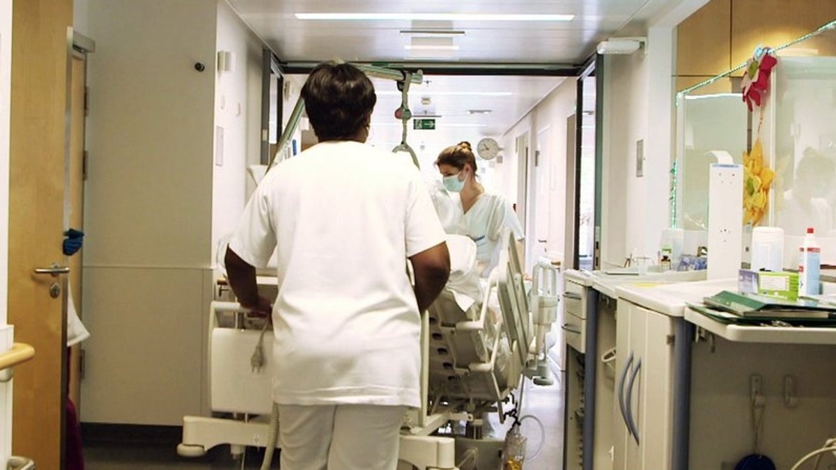 Pflegekräfte schieben einen Patienten im Krankenbett durch einen Flur im Krankenhaus