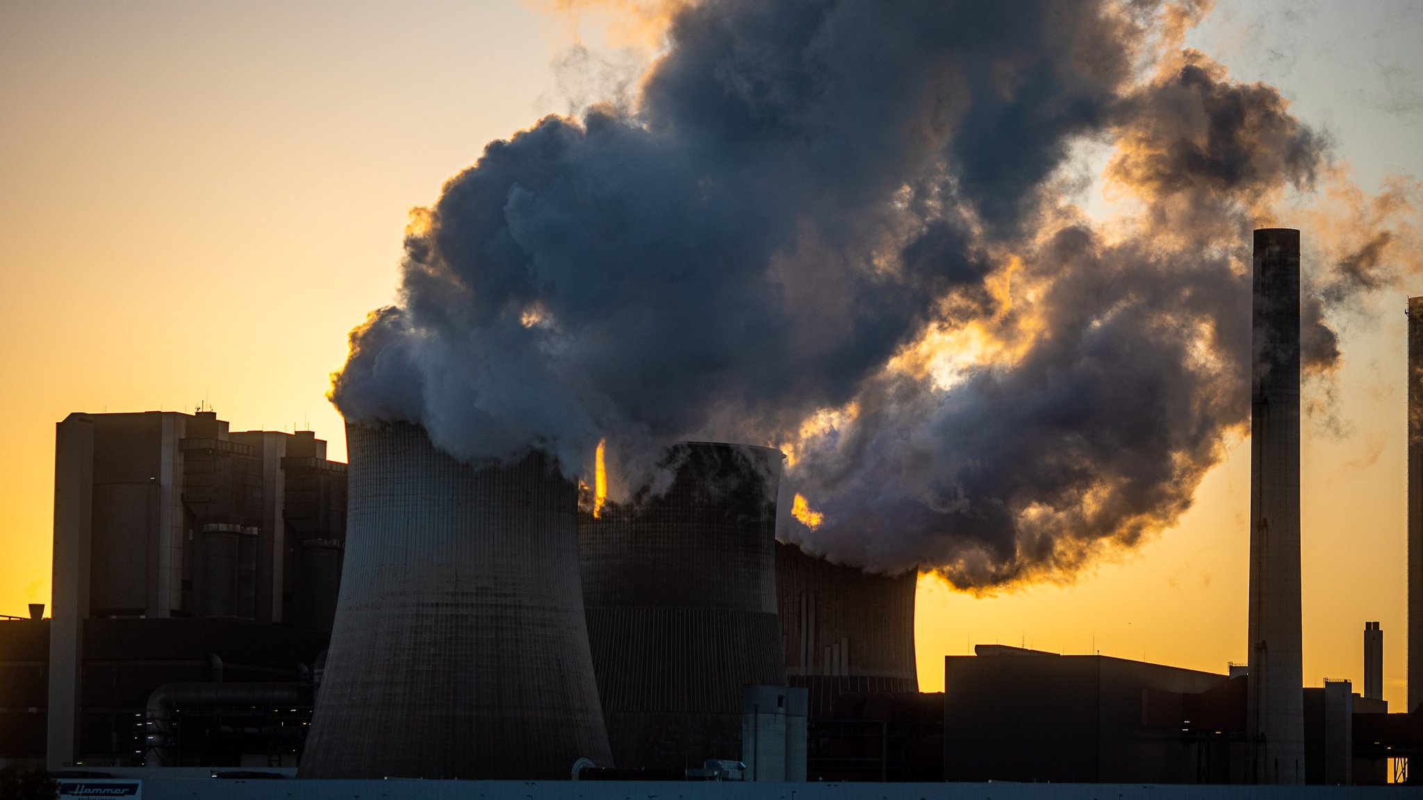 Kraftwerk mit rauchenden Schloten vor Sonnenaufgang.