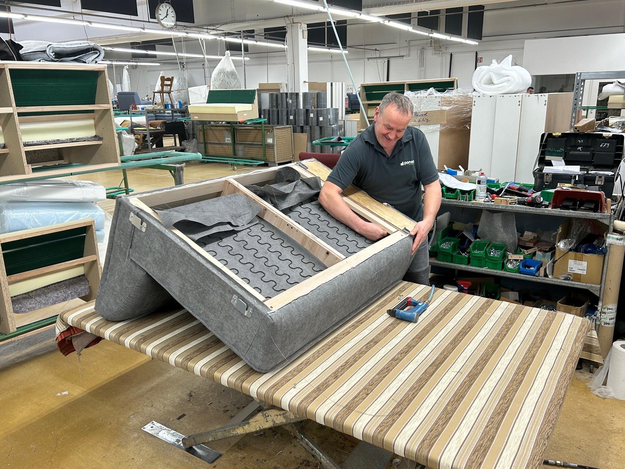 Ein Mitarbeiter eine Möbelherstellers baut ein Sofa zusammen.