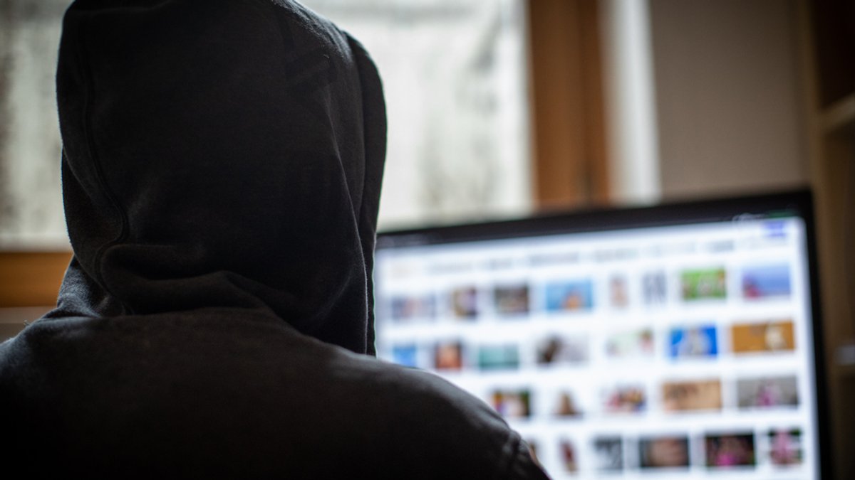Mann mit Kapuze über dem Kopf sitzt vor einem Monitor, auf dem pornografische Bilder zu sehen sind