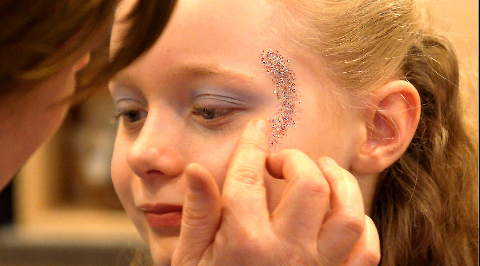 Ein Mädchen wird mit Glitter geschminkt.