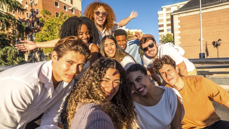 Frontalansicht einer multiethischen fröhlichen Freundesgruppe. Sie nehmen ein Selfie zusammen in der Stadt auf. | Bild: picture alliance / imageBROKER | Unai Huizi Frontalansicht einer multiethischen fröhlichen Freundesgruppe. Sie nehmen ein Selfie zusammen in der Stadt auf.