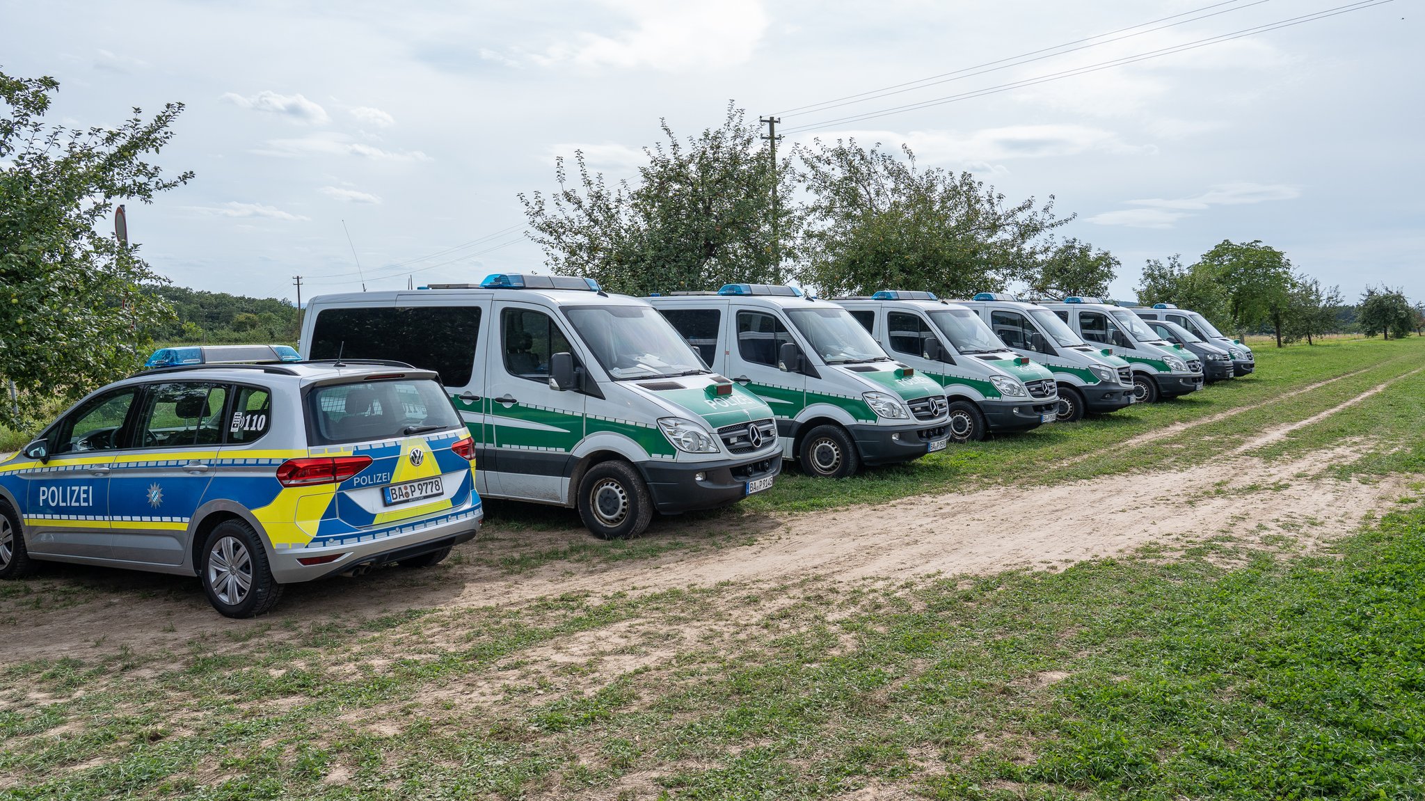 Polizeibusse stehen auf einem Feldweg. 