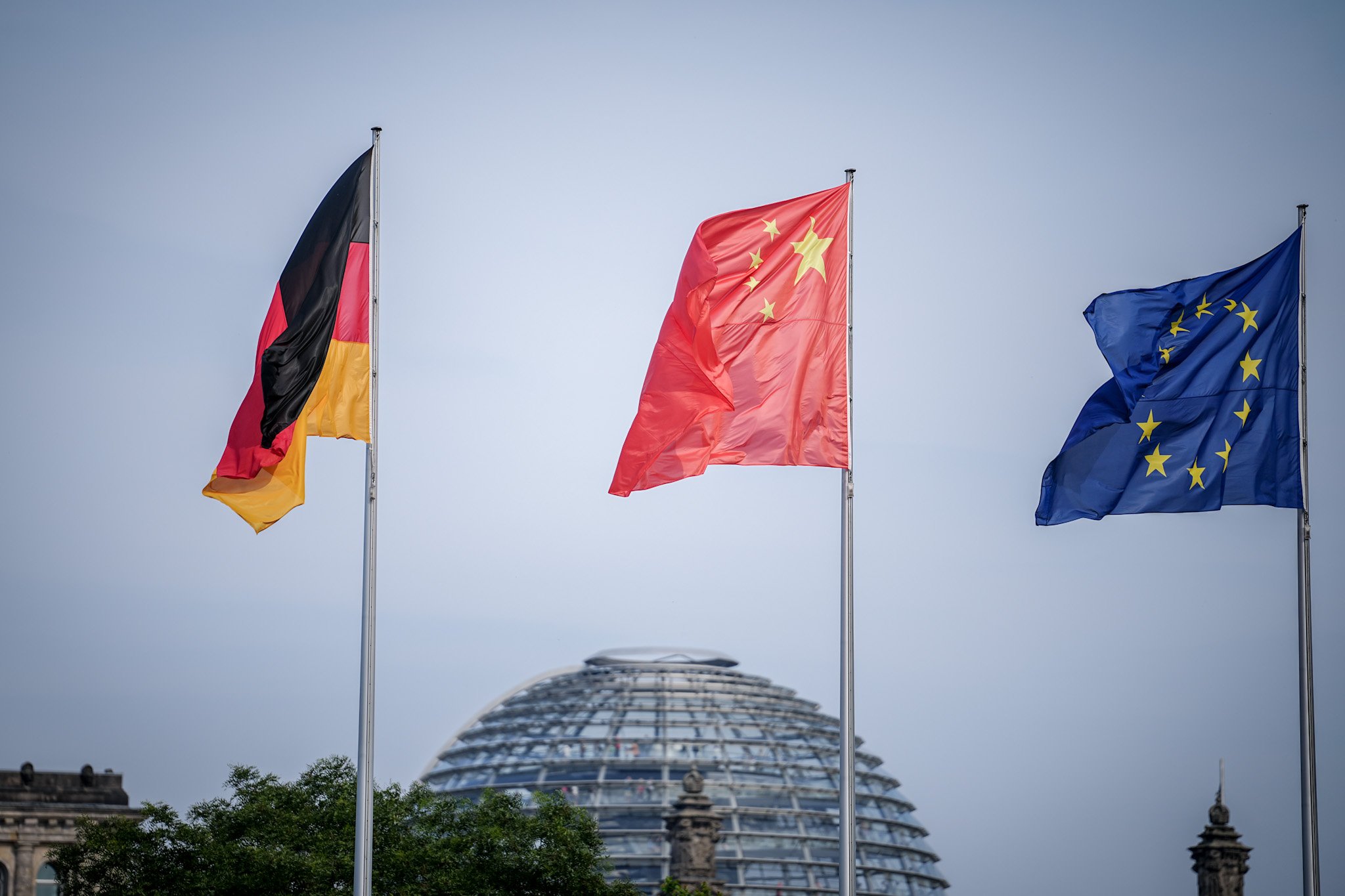 ARCHIV - 19.06.2023, Berlin: Die Flaggen von Deutschland, China und der EU wehen zum Auftakt des Deutschland-Besuchs der chinesischen Regierung im Wind vor dem Bundeskanzleramt, im Hintergrund die Kuppel des Reichstagsgebäudes. EU-Unternehmen können der chinesischen Wirtschaft einer Analyse zufolge dringend benötigten Wettbewerb und Technologie bieten. Dies setze allerdings einen offenen Markt und gleiche Wettbewerbsbedingungen voraus, schrieb die Europäische Handelskammer in einem am Dienstag veröffentlichten Positionspapier. (zu dpa «Handelskammer fordert gerechtere Bedingungen für EU-Firmen in China») Foto: Kay Nietfeld/dpa +++ dpa-Bildfunk +++