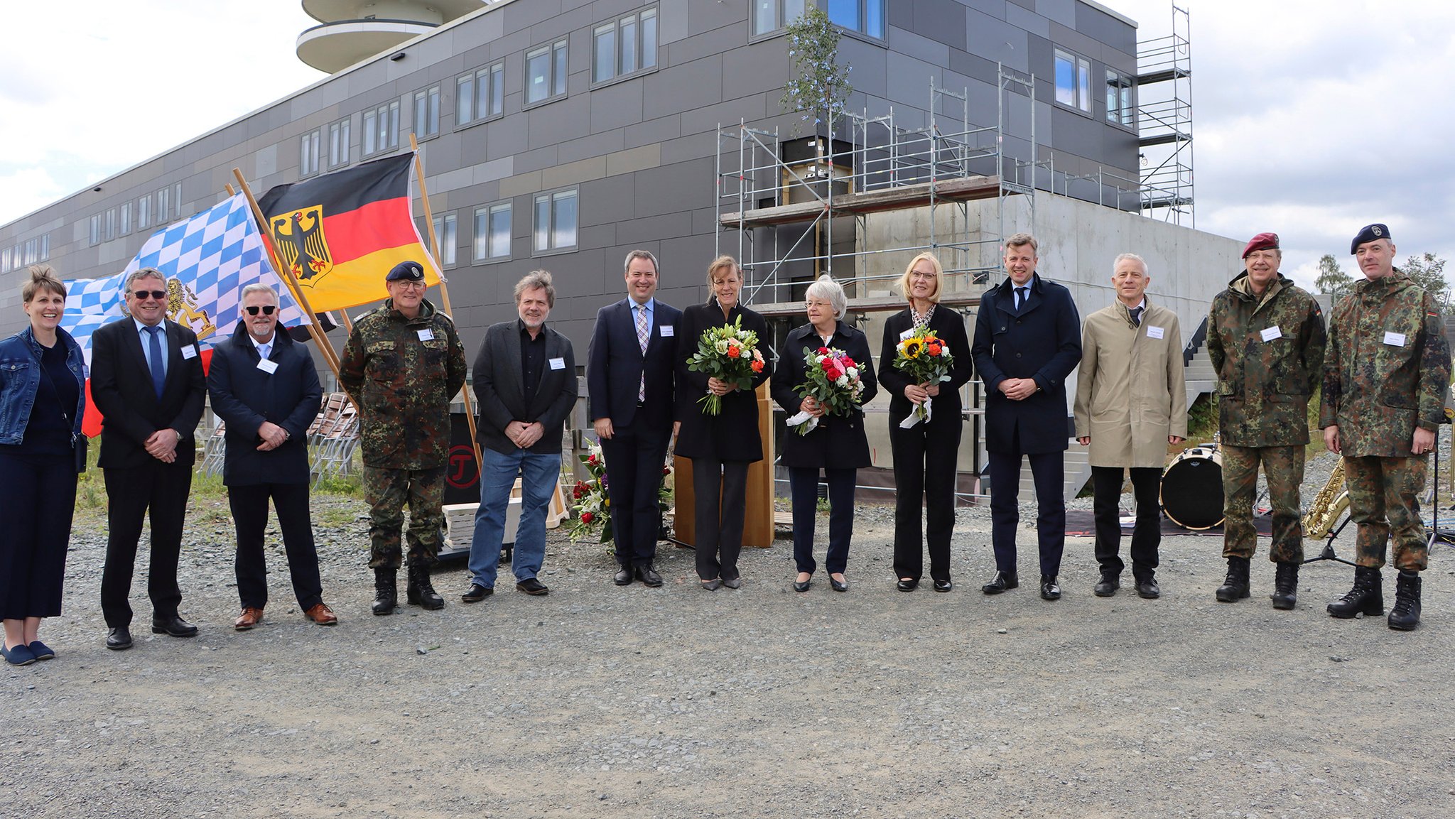 Mehrere Persönlichkeiten aus Politik und Wirtschaft stehen, teils mit Blumensträußen, für ein Gruppenbild vor dem neuen Gebäude für technische Aufklärung der Bundeswehr. 