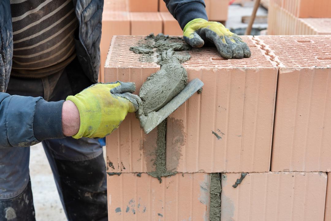 Ein Maurer arbeitet mit einem Spachtel und Beton an einer Ziegelmauer 