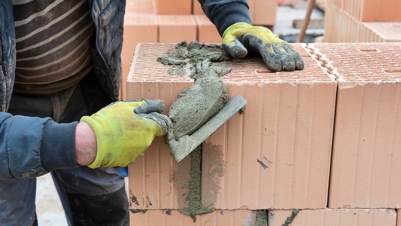 Ein Maurer arbeitet mit einem Spachtel und Beton an einer Ziegelmauer | Bild: colourbox.com/Wolfgang Filser Ein Maurer arbeitet mit einem Spachtel und Beton an einer Ziegelmauer