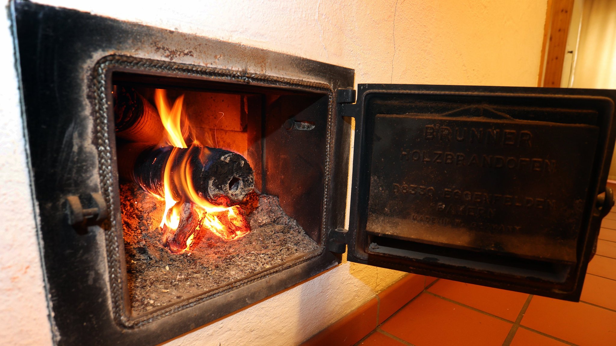 Ein Holzofen wird vom Hausflur aus mit Holzbriketts geheizt.