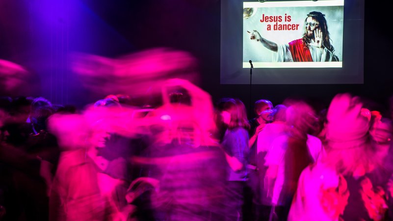 Während auf einer digitalen Anzeige der Spruch "Jesus is a dancer" aufleuchtet, tanzen Menschen trotz des Tanzverbots an Karfreitag in einem Club. | Bild: picture alliance/dpa | Christoph Schmidt Während auf einer digitalen Anzeige der Spruch "Jesus is a dancer" aufleuchtet, tanzen Menschen trotz des Tanzverbots an Karfreitag in einem Club.