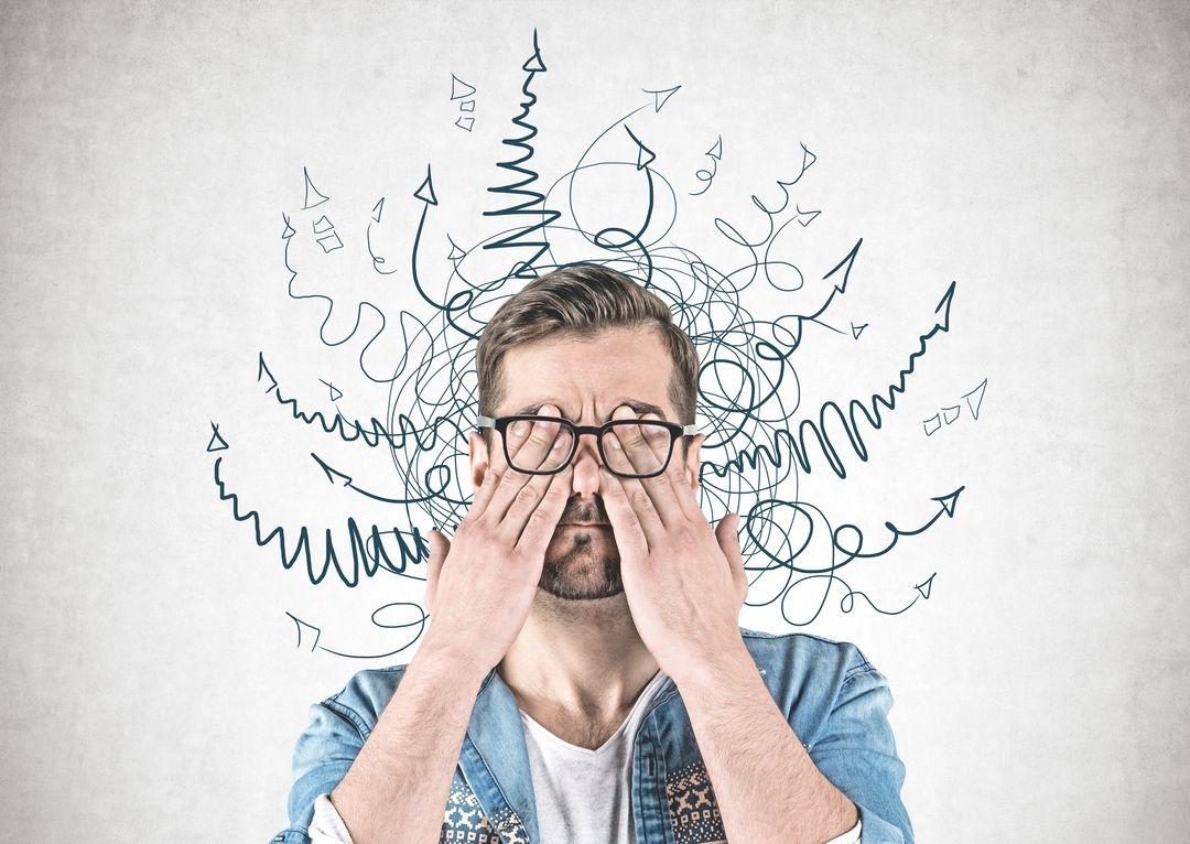 Ein Mann hält sich die Augen zu, hinter ihm ein Wirrwarr