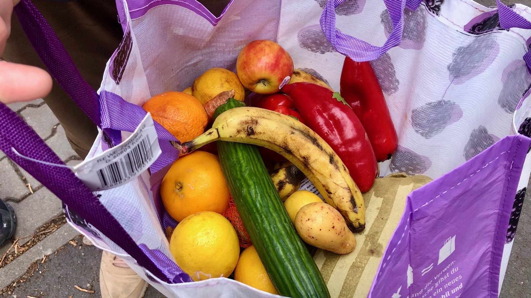 Eine Tüte voll mit Orangen, Spitzpaprika, Gurken, Bananen und Äpfeln.