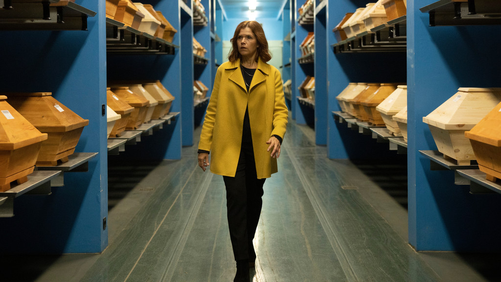 Anke Engelke geht als Karla Fazius durch ein Lager mit Särgen in der Netflix-Serie "Das letzte Wort" 