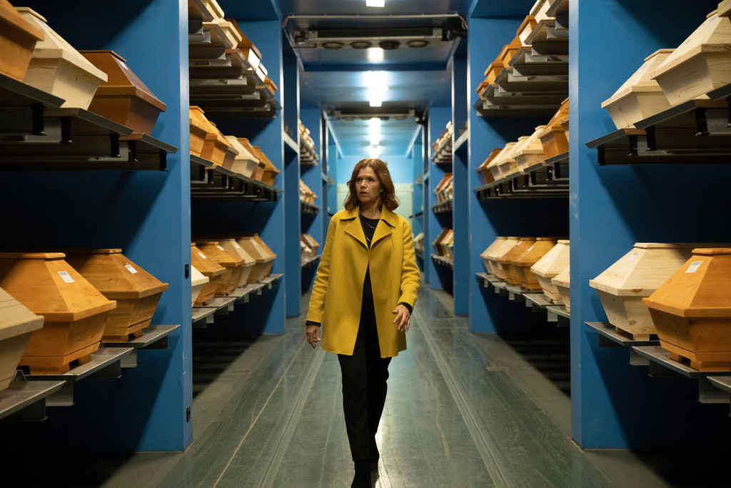 Anke Engelke geht als Karla Fazius durch ein Lager mit Särgen in der Netflix-Serie "Das letzte Wort" 