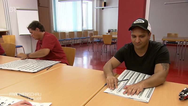 Eine Frau und ein Mann testen die Wahlschablone für Blinde