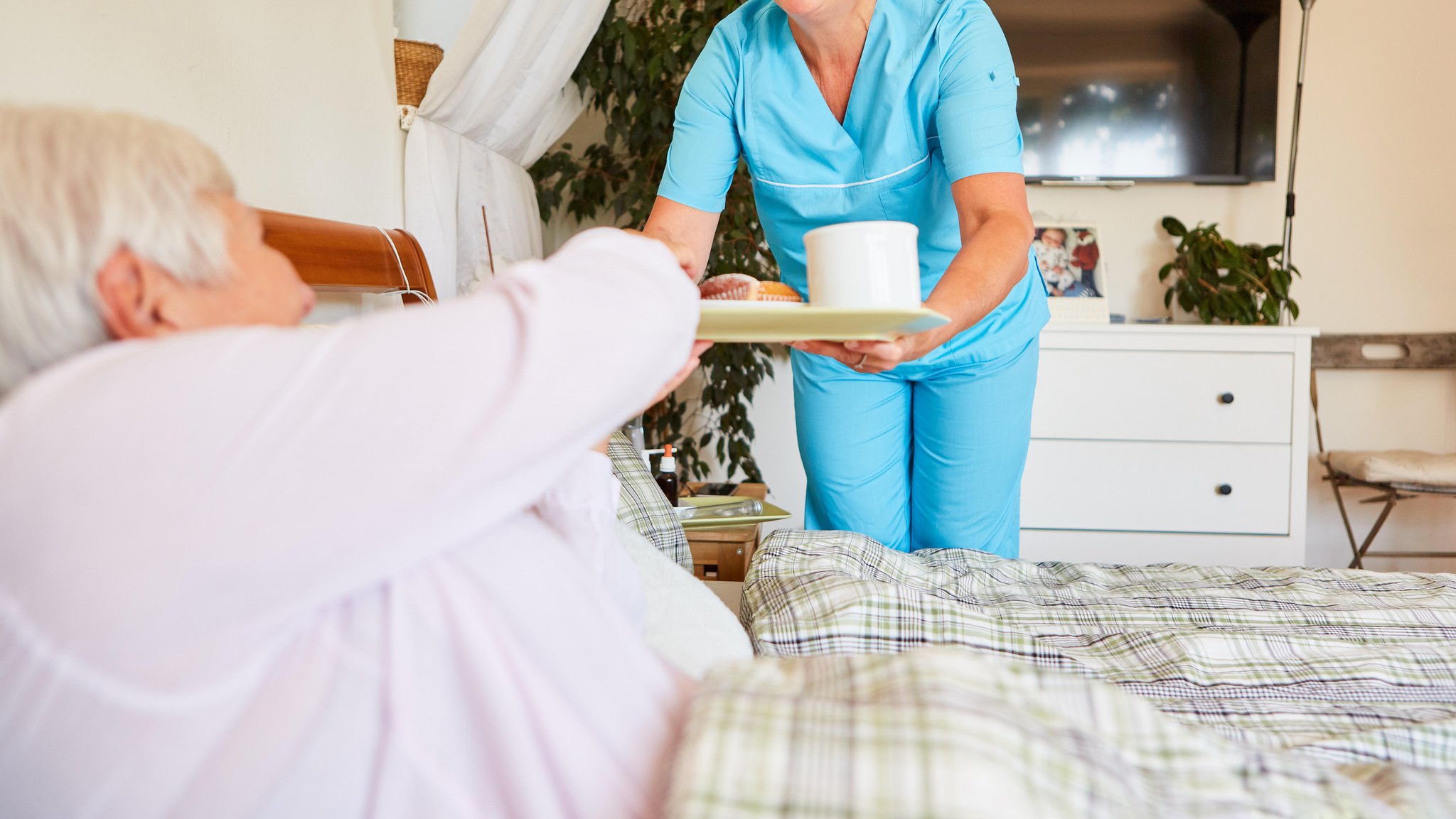 Eine Pflegerin bringt einer Seniorin Frühstück ans Bett 