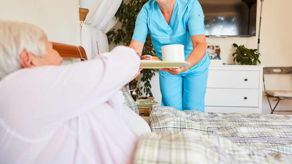 Eine Pflegerin bringt einer Seniorin Frühstück ans Bett 
