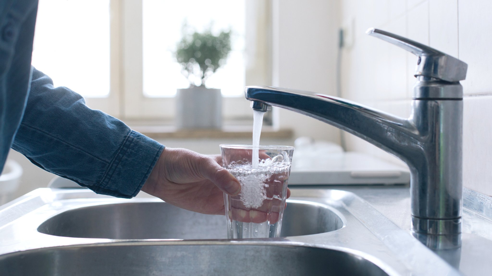 Jemand füllt Wasser aus der Leitung in ein Glas