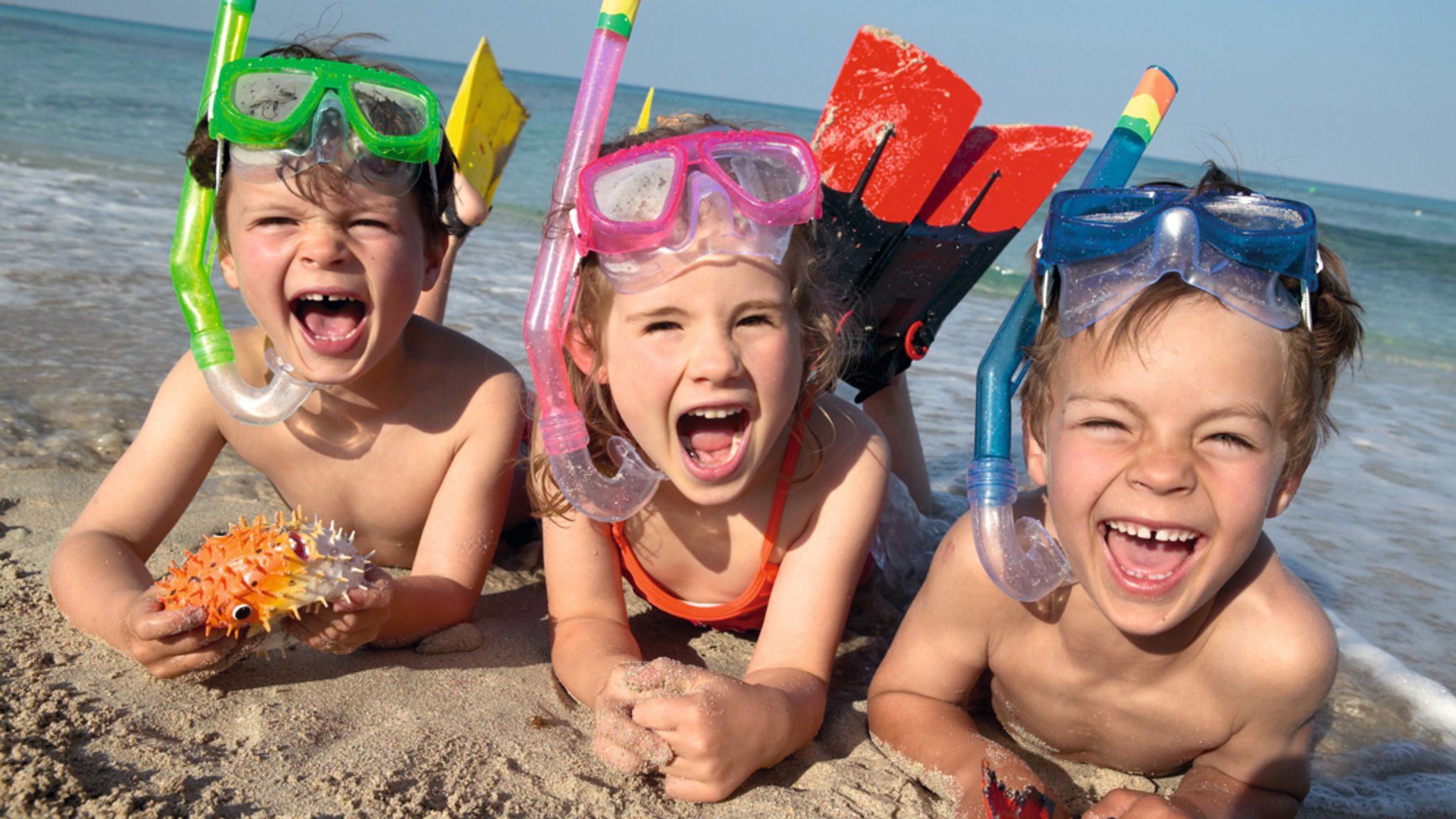 Drei Kinder mit Taucherbrillen und Schnorchel am Strand.