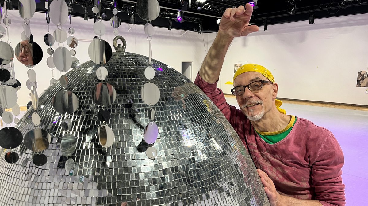 Der Choreograph lehnt sich an eine silberne Disco-Kugel